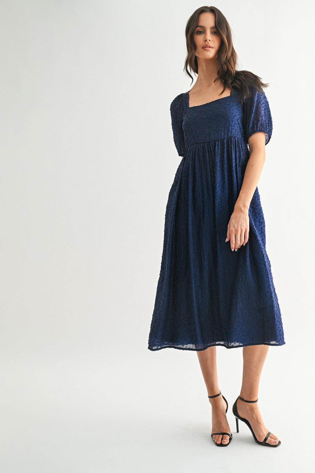 woman wearing a navy blue textured midi dress with a square neckline and puff sleeves