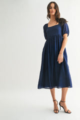 woman wearing a navy blue textured midi dress with a square neckline and puff sleeves