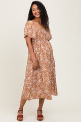 woman wearing a brown floral print maternity dress with short sleeves and a smocked bodice, showing her baby bump