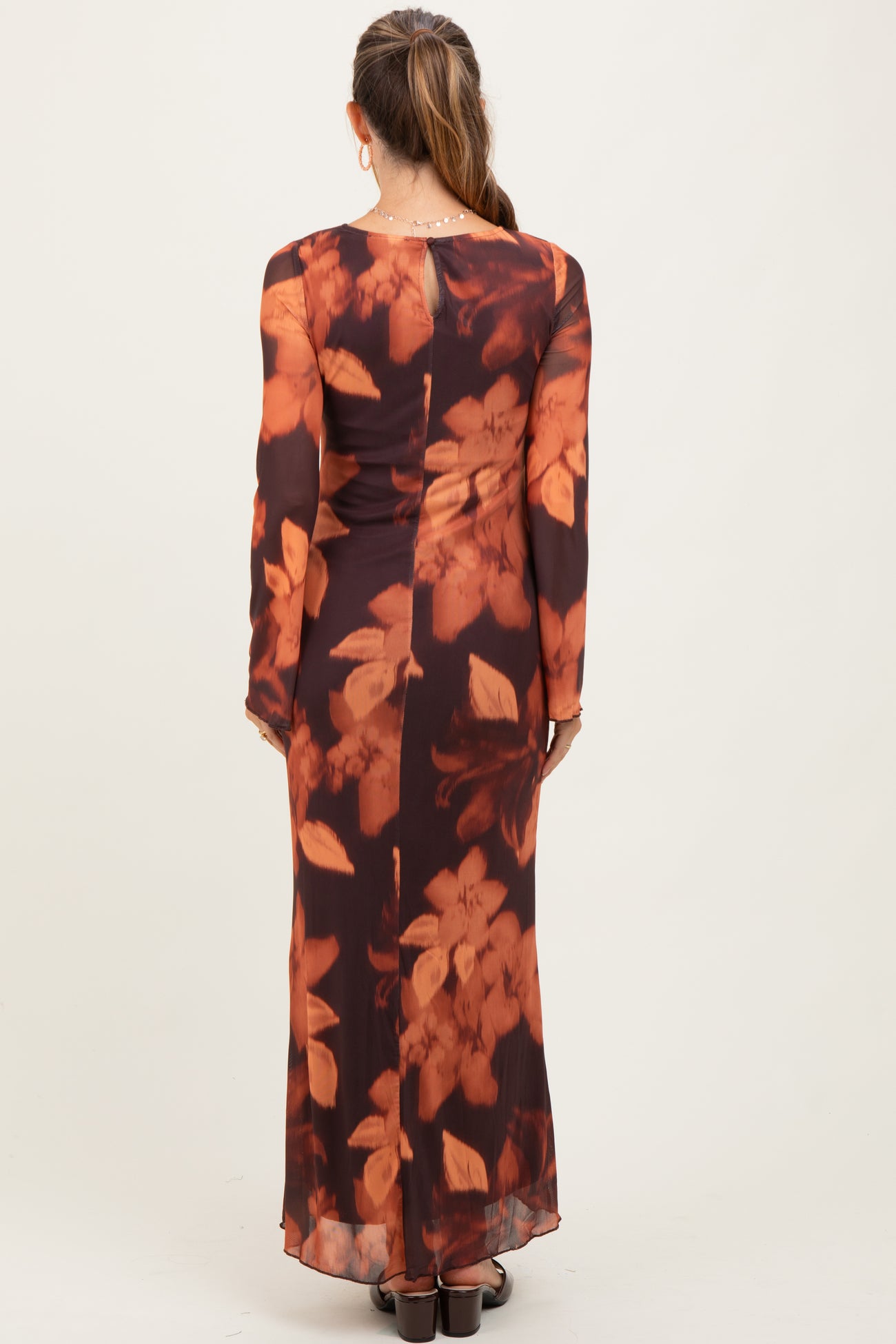woman wearing a long sleeve brown floral maternity dress with a fitted silhouette and a flowing skirt from the back
