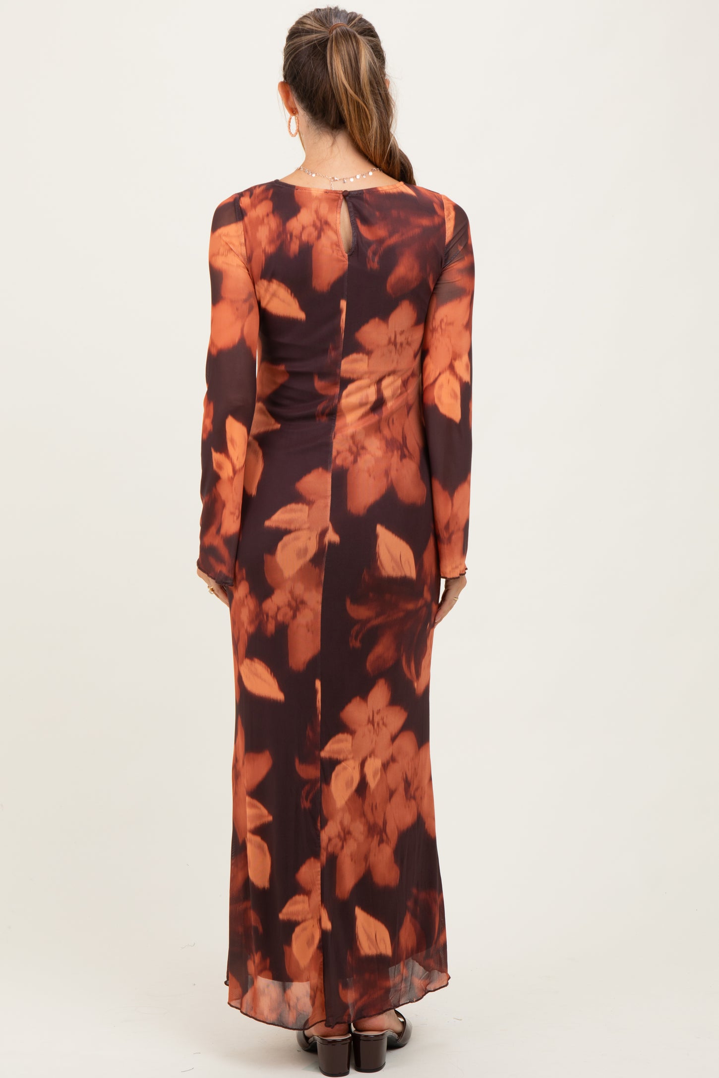 woman wearing a long sleeve brown floral maternity dress with a fitted silhouette and a flowing skirt from the back