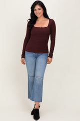 woman wearing a maroon ribbed long sleeve top with a square neckline and distressed light blue flared jeans