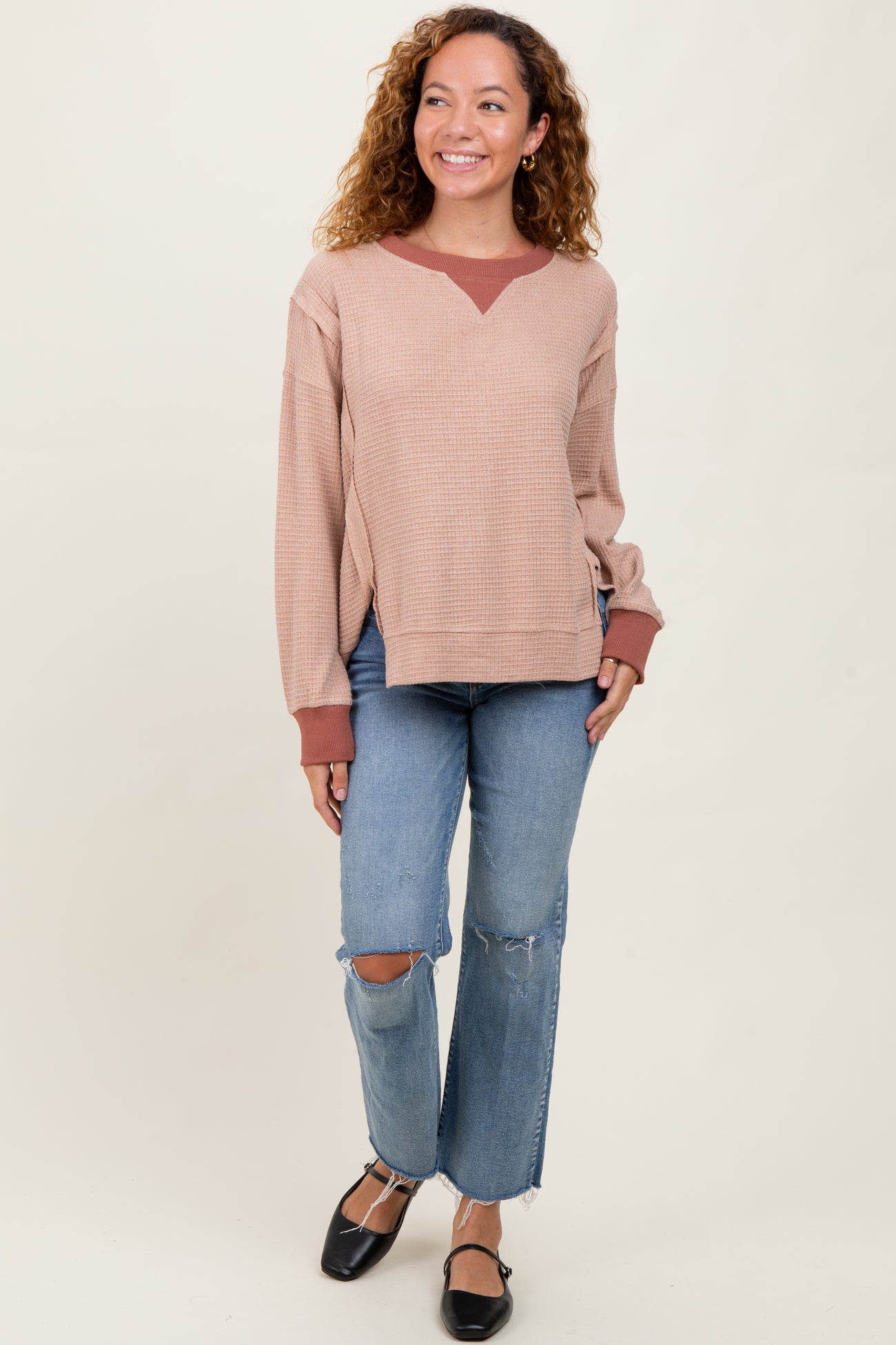 woman wearing a blush pink waffle knit sweater with rust accents and distressed light blue flared jeans