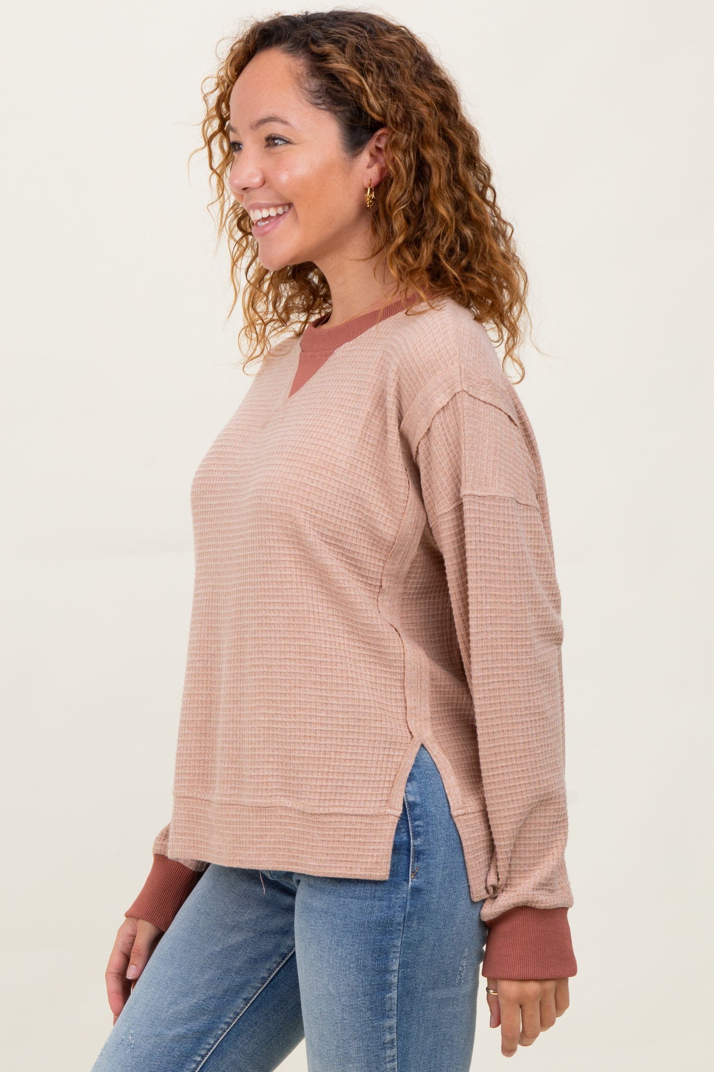 woman wearing a beige waffle knit pullover with burgundy accents and side slits, paired with light blue jeans
