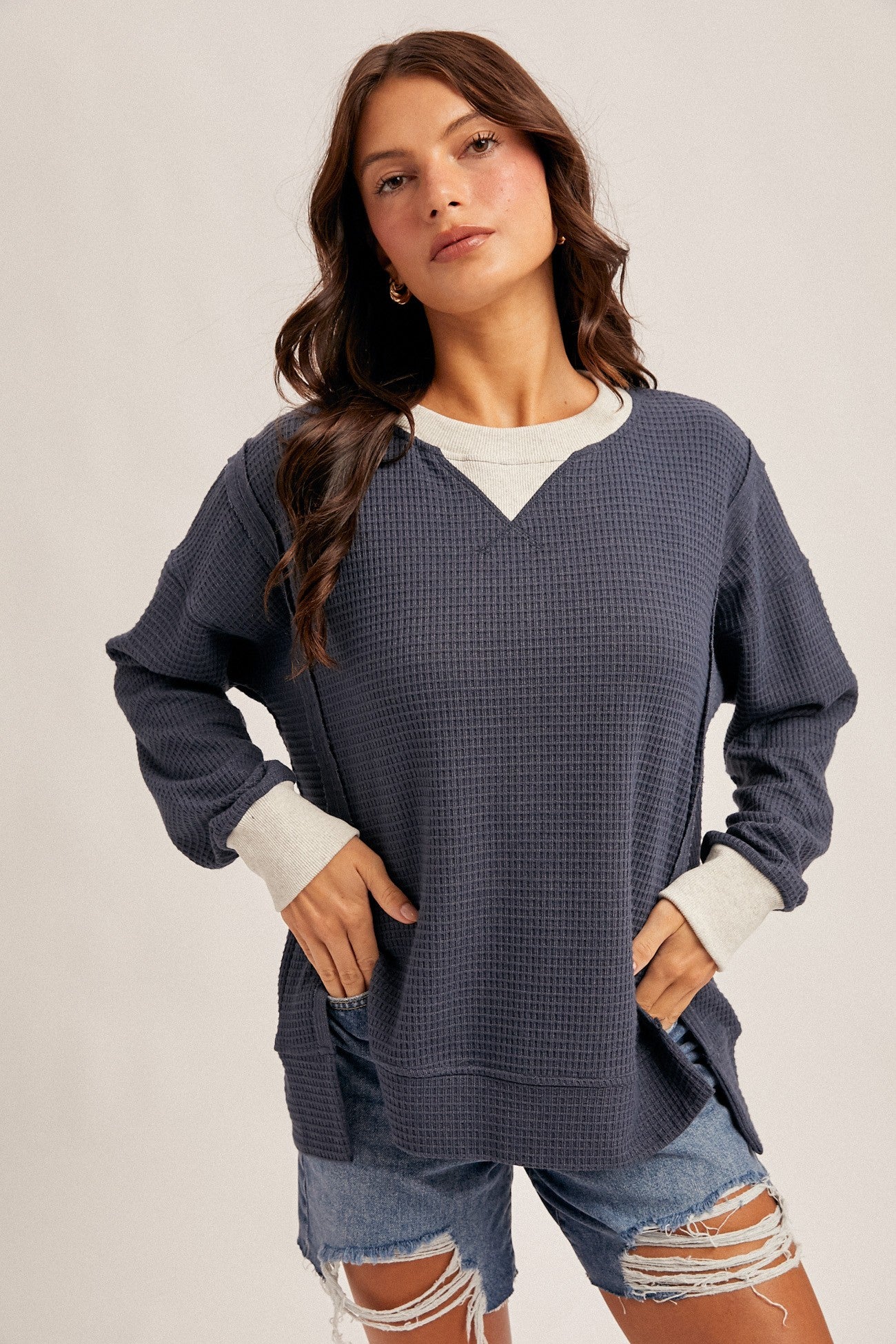 woman wearing a navy blue waffle knit long sleeve top with a white neckline and distressed denim shorts