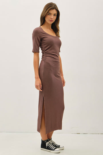 woman wearing a brown fitted midi dress with short sleeves and side slit, paired with black Converse sneakers