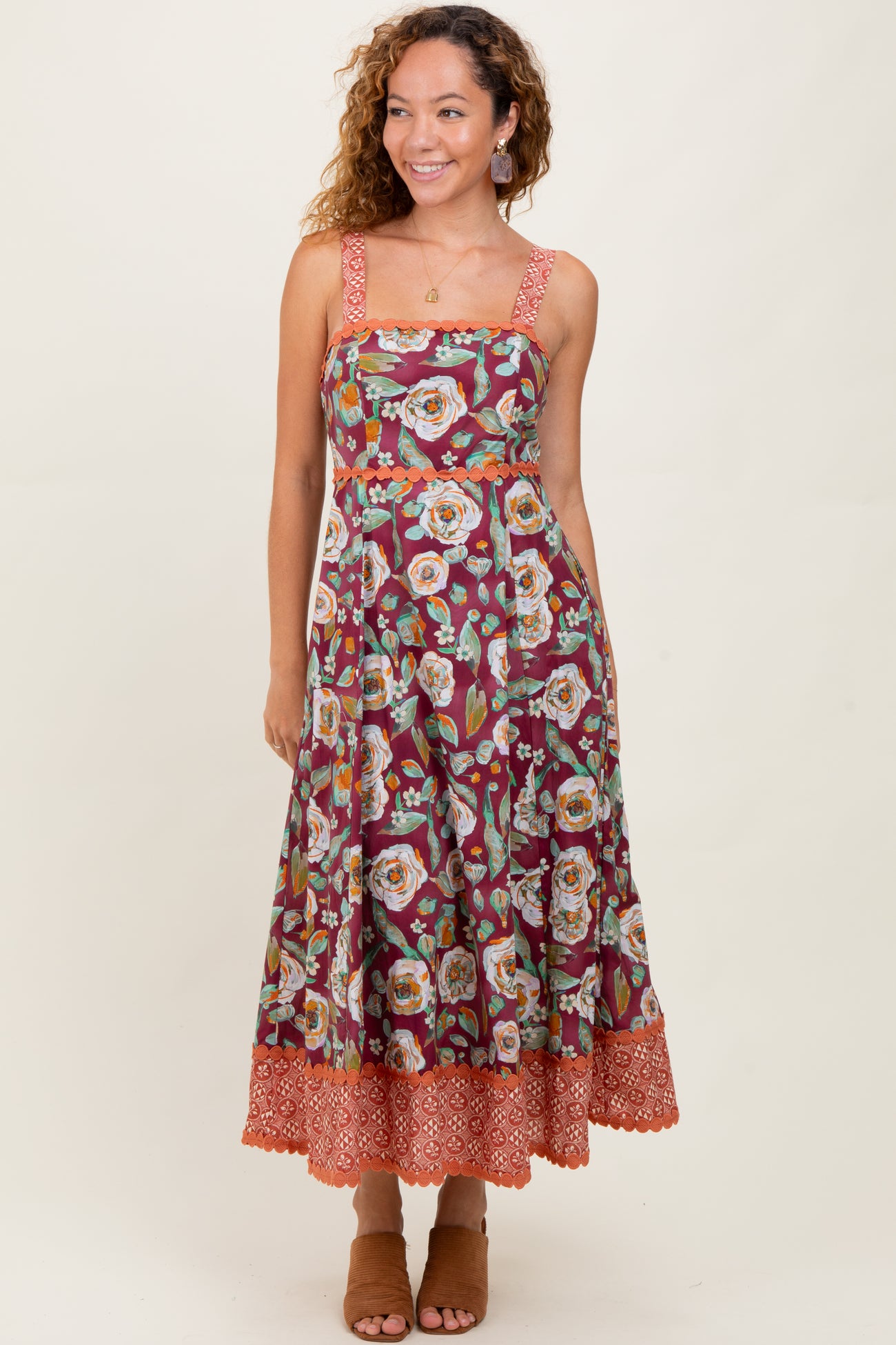woman wearing a burgundy floral midi dress with thick straps and a tiered hemline, styled with tan block heel sandals