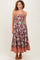 woman wearing a burgundy floral midi dress with thick straps and a tiered hemline, styled with tan block heel sandals