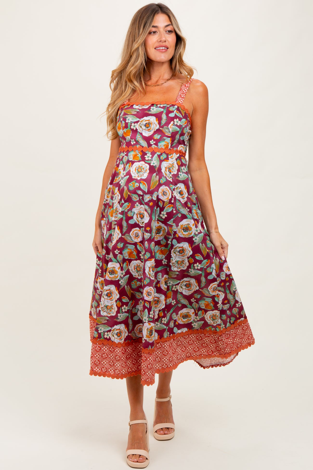 woman wearing a floral burgundy maternity dress with orange trim and an elastic waistband