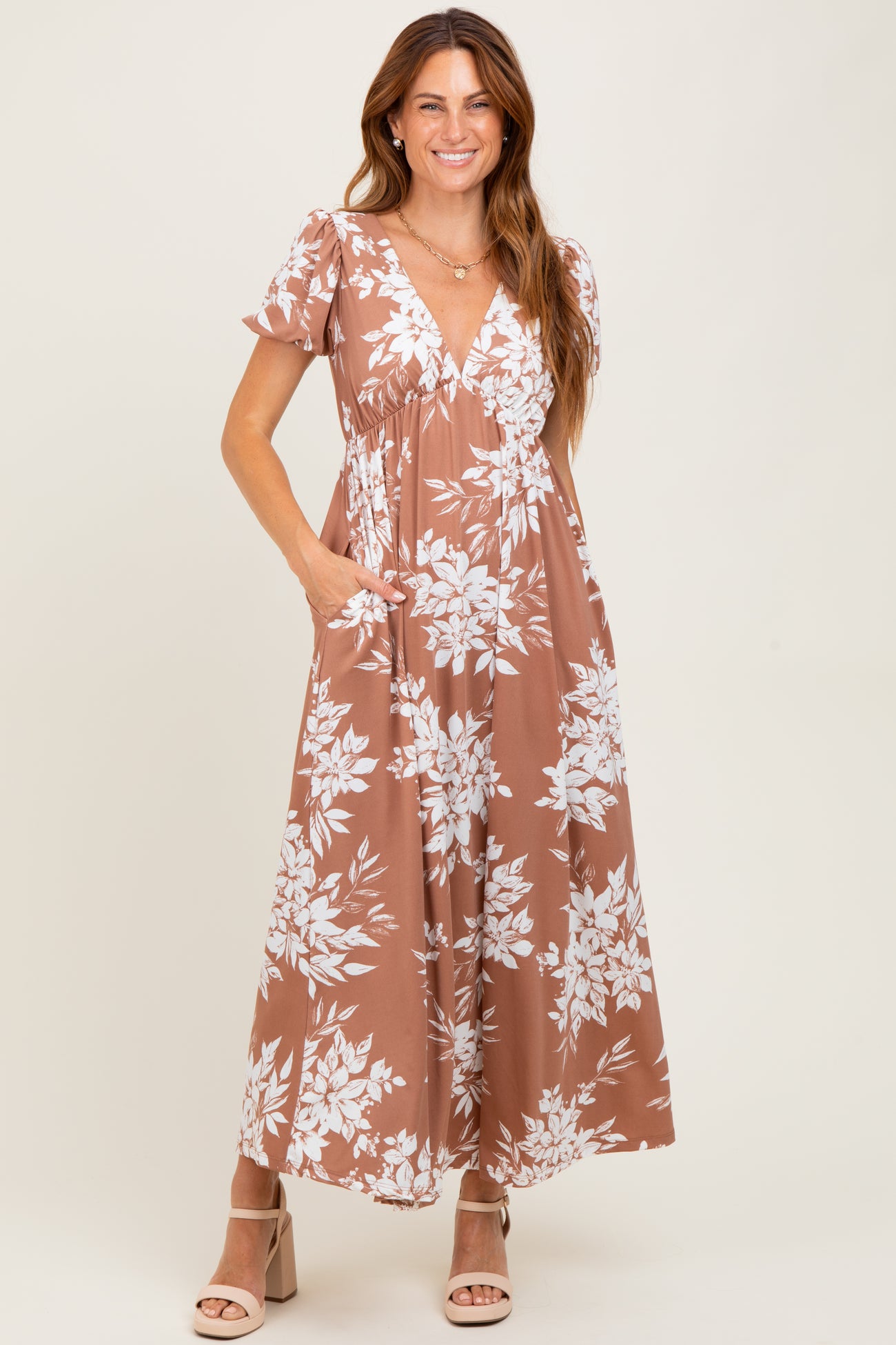 woman wearing a brown floral maxi dress with a v-neckline and short sleeves, featuring pockets and a relaxed fit