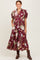 woman wearing a burgundy floral maxi dress with puff sleeves and button details, paired with brown ankle boots