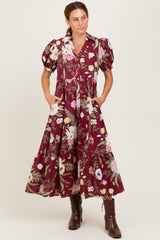 woman wearing a burgundy floral maxi dress with puff sleeves and pockets, standing in brown ankle boots