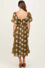 woman wearing a green floral maternity dress with puff sleeves and a smocked bodice, showcasing her baby bump from the back