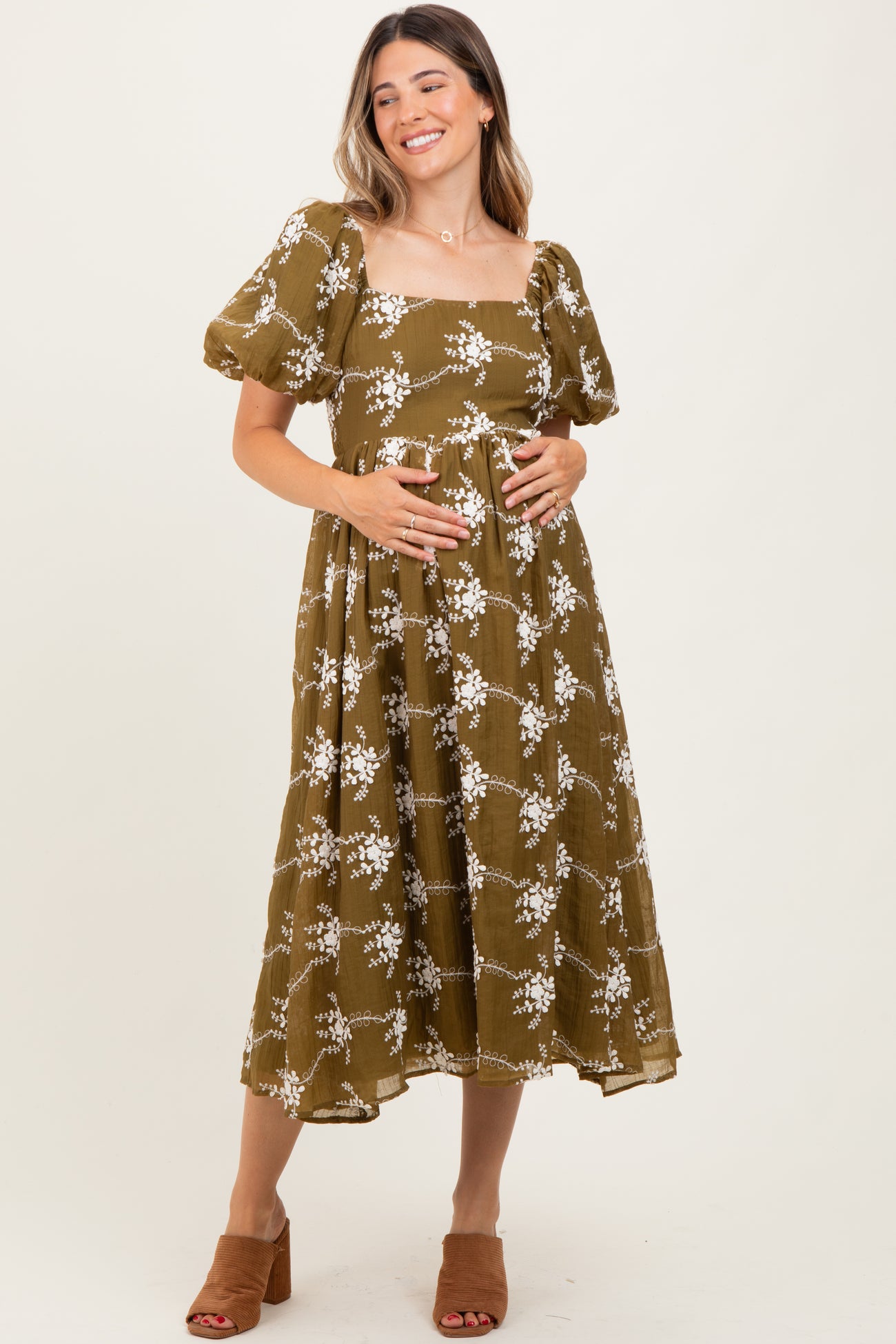 woman wearing a brown floral maternity dress with puff sleeves and holding her baby bump