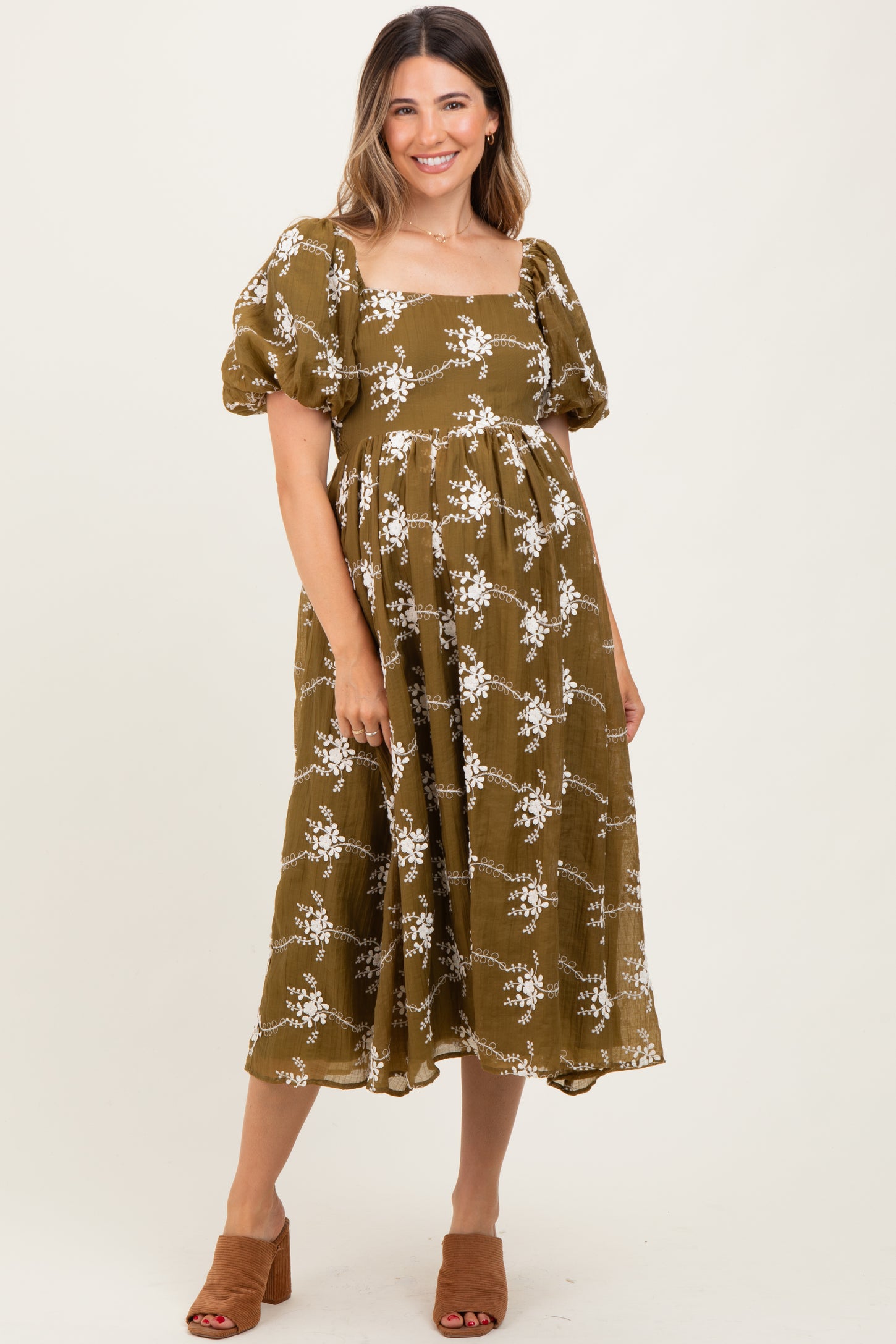 woman wearing a green floral maternity dress with short puff sleeves and a flowy mid-length skirt, showing her baby bump