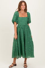 woman wearing a green midi dress with puff sleeves and square neckline, standing and smiling