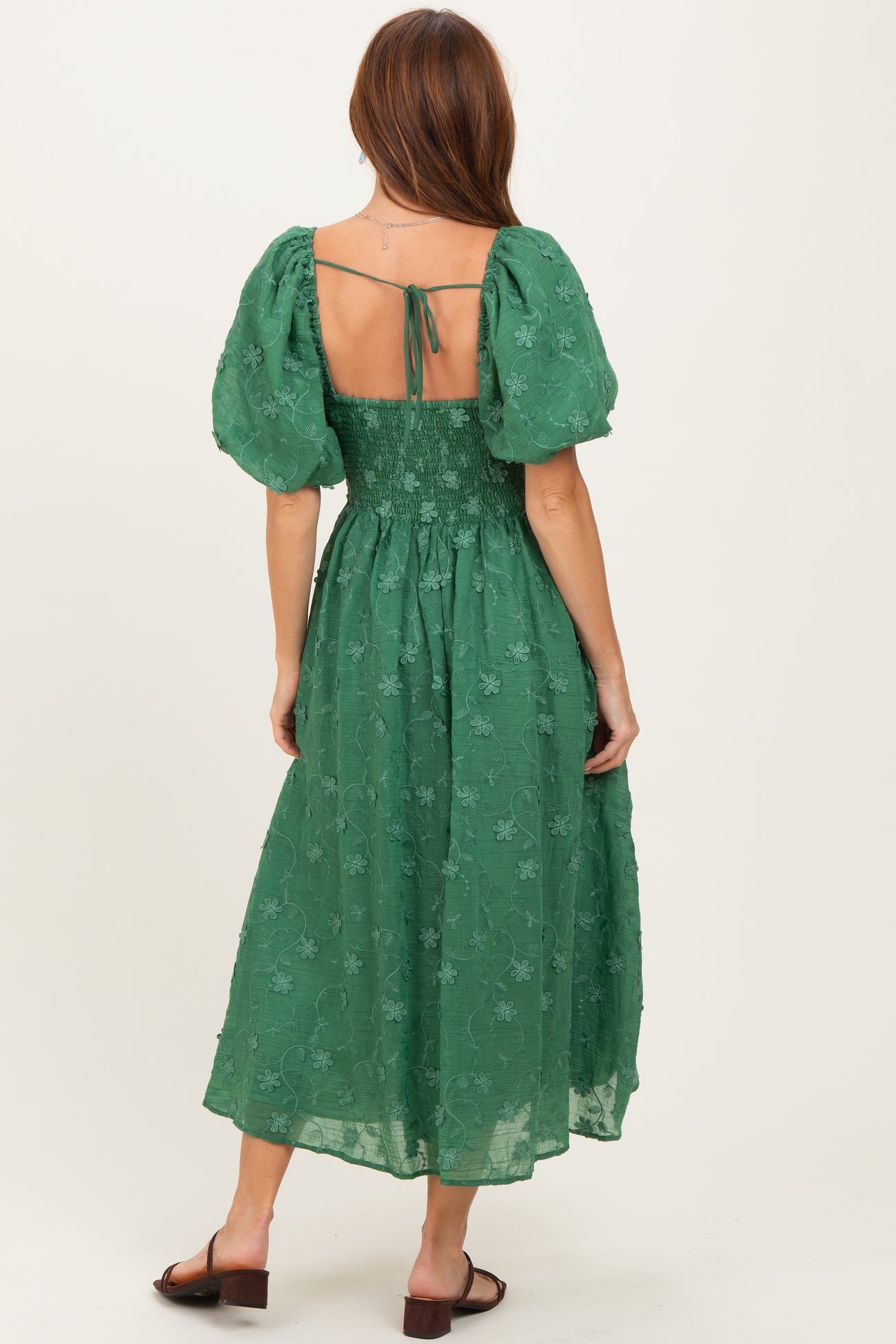 woman wearing a green floral embroidered midi dress with puff sleeves and an open back