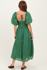woman wearing a green floral embroidered midi dress with puff sleeves and an open back