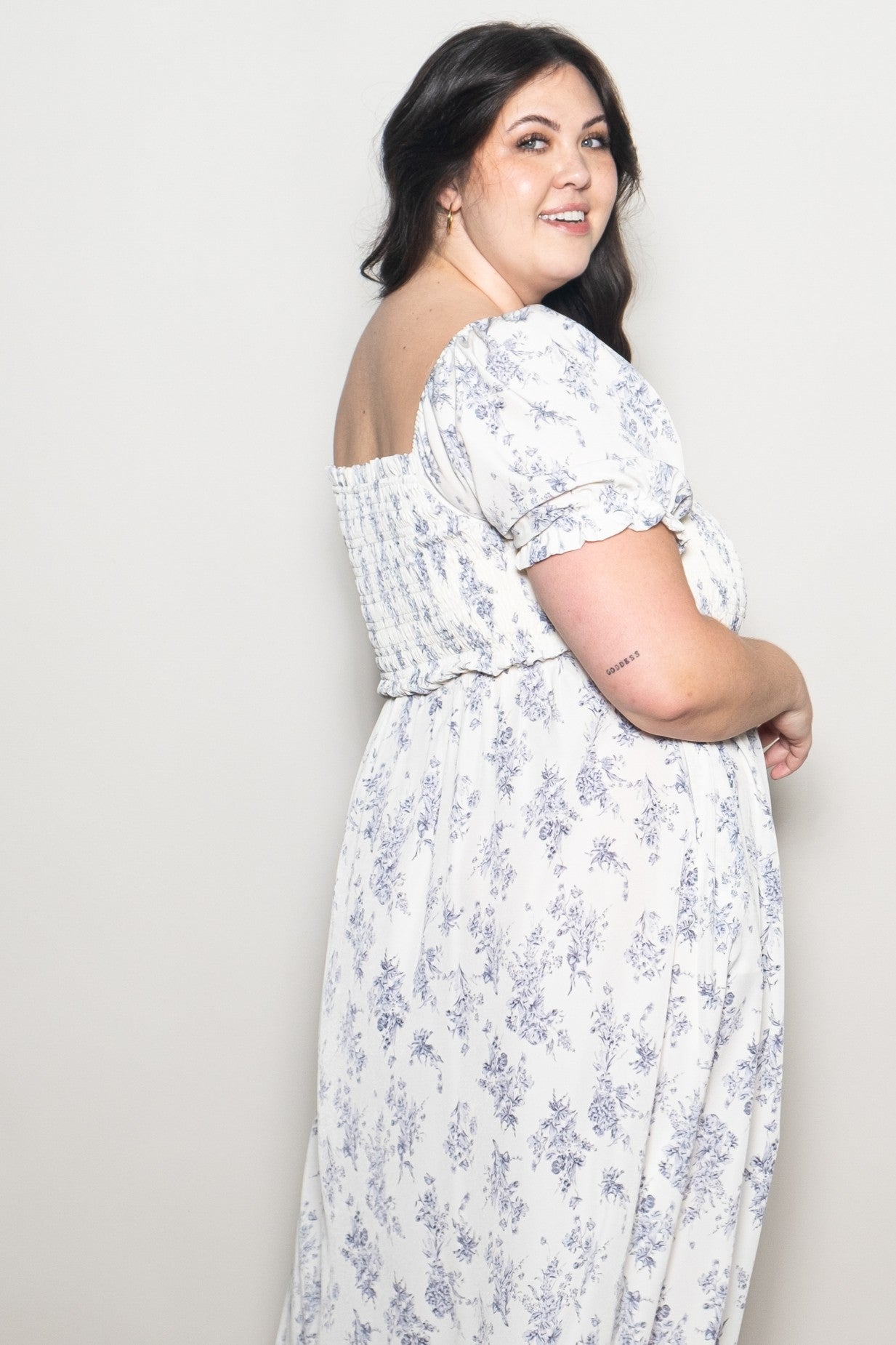 woman wearing a white floral print plus size maxi dress with puff sleeves and smocked back, smiling over her shoulder