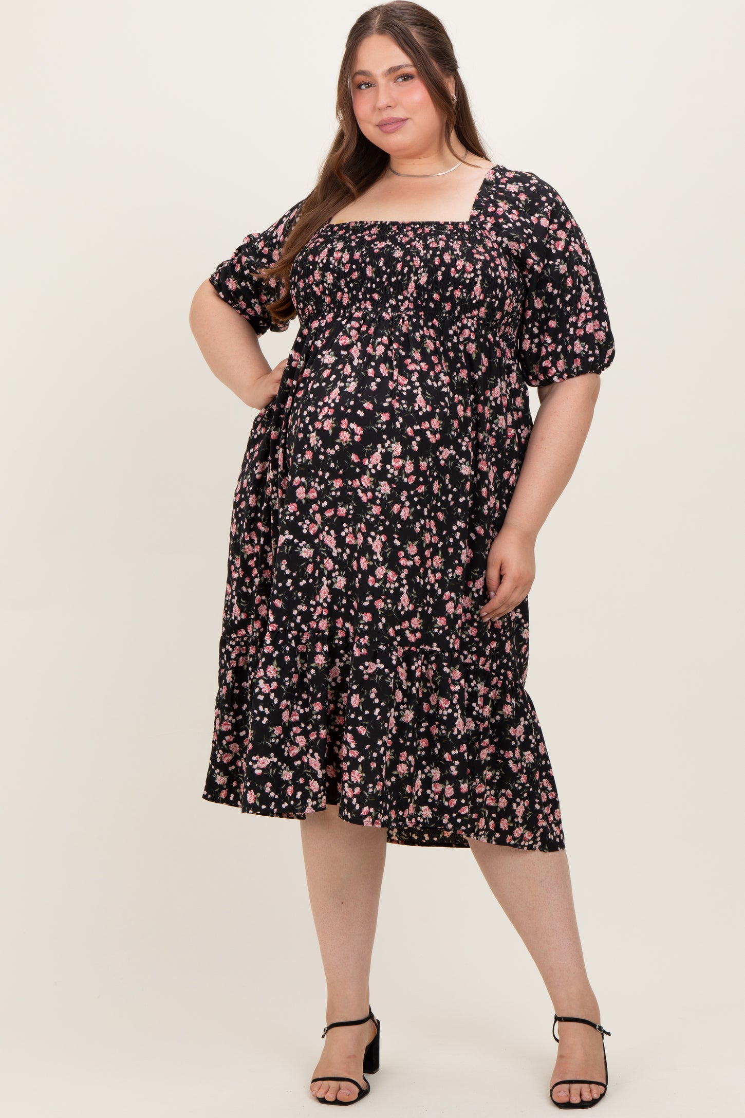 woman wearing a black floral maternity plus dress with puff sleeves and a tiered ruffle hem, showing her baby bump