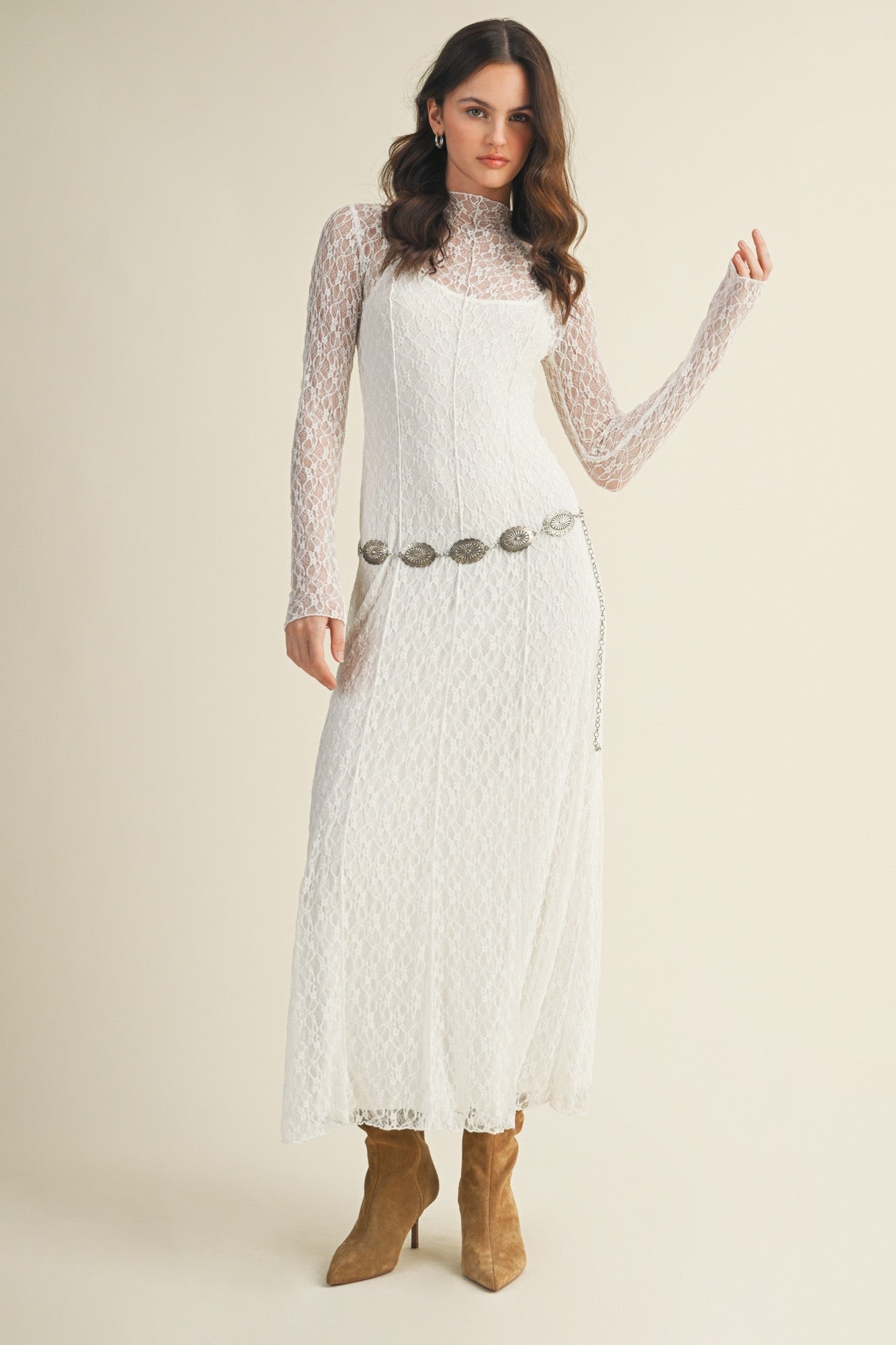woman wearing a white lace long sleeve maxi dress with a silver belt and brown heeled boots