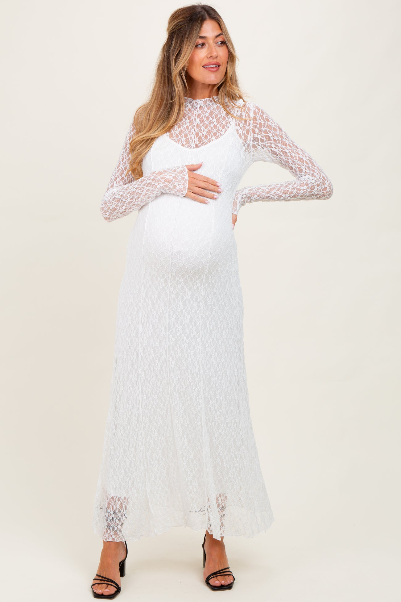 woman wearing a white lace long sleeve maternity dress and holding her baby bump