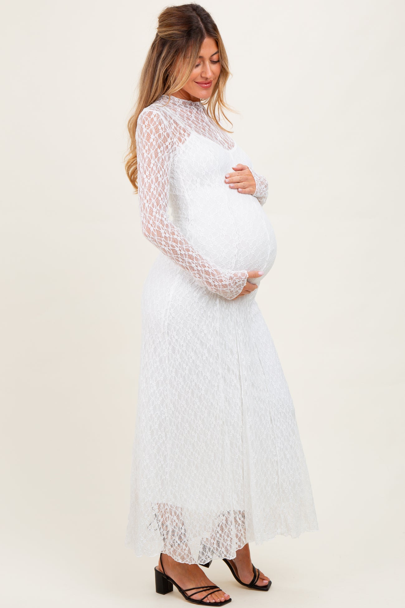 woman wearing a white long sleeve lace maternity dress and holding her baby bump