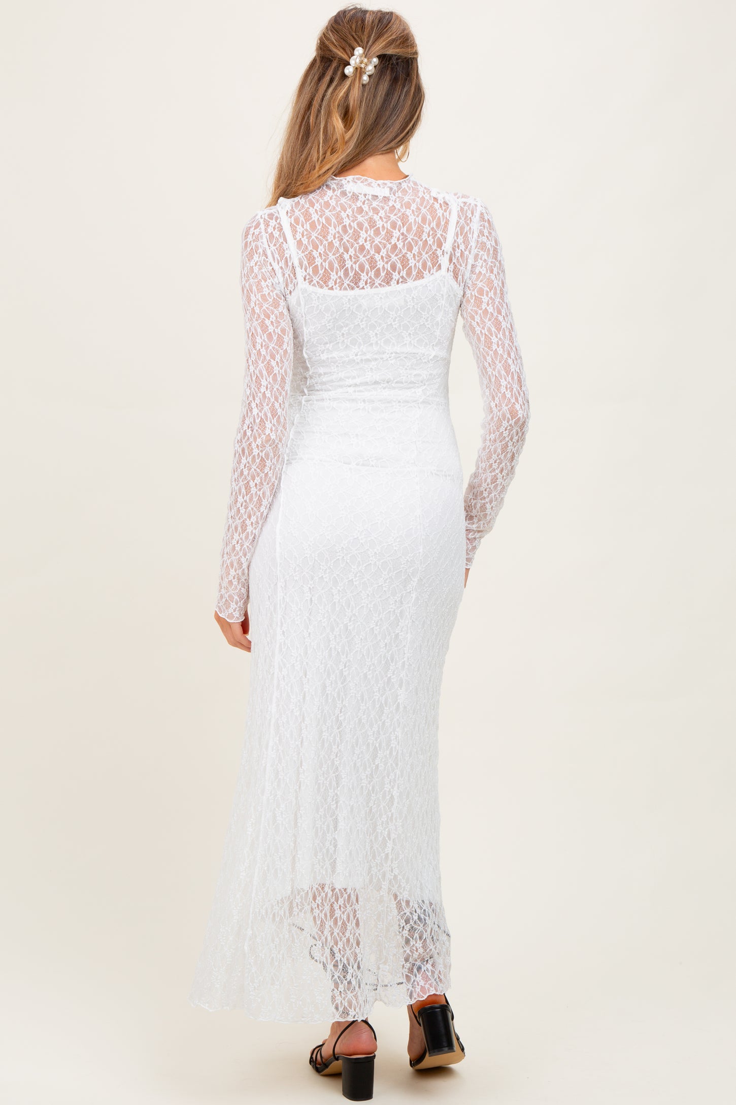 woman wearing a white lace maternity dress with long sleeves and a flowing silhouette, showing a baby bump from the back