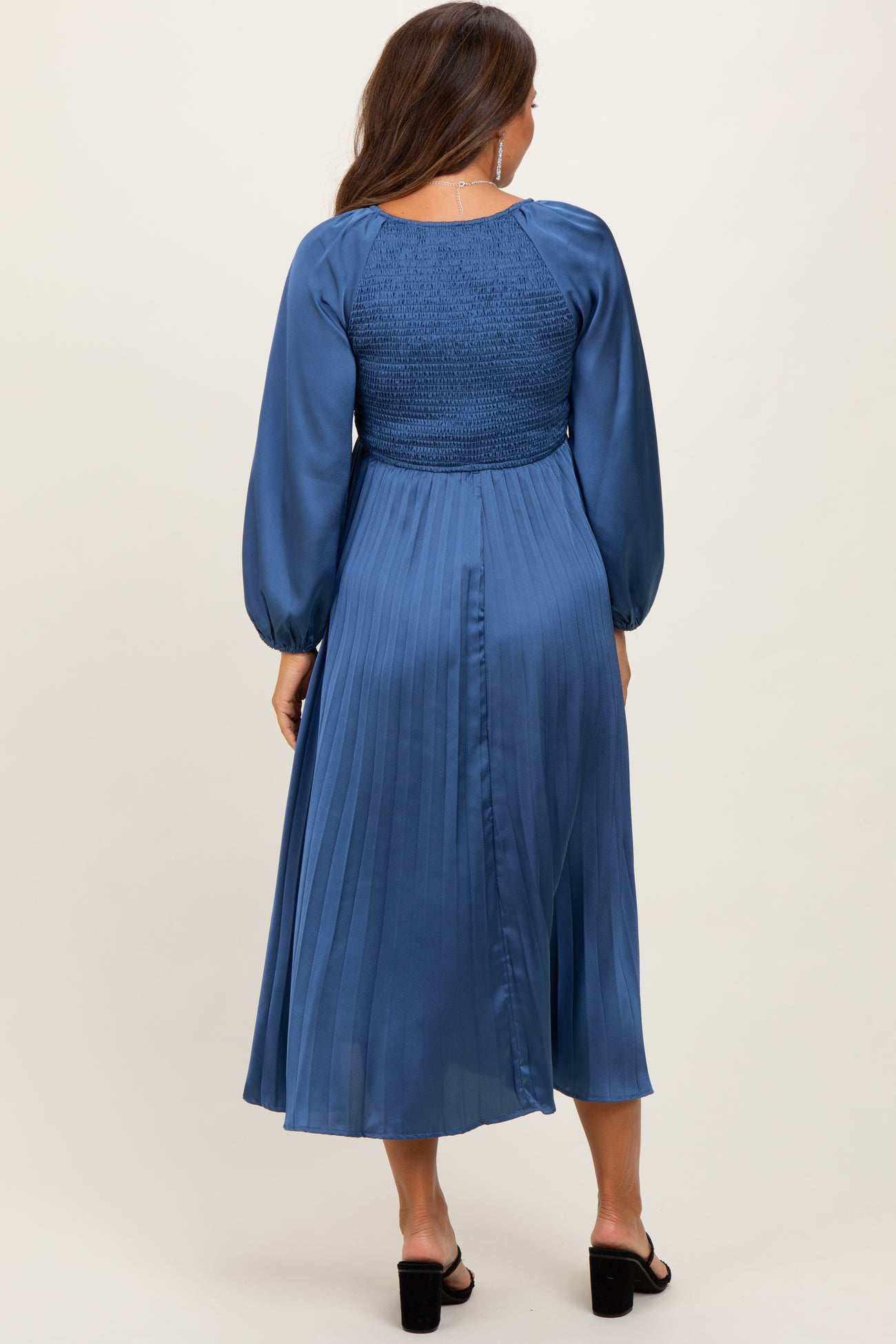 woman wearing a blue pleated maternity dress with a smocked bodice and long puff sleeves, showing a baby bump