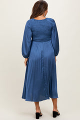 woman wearing a blue pleated maternity dress with a smocked bodice and long puff sleeves, showing a baby bump