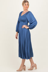 woman wearing a blue pleated long sleeve dress with a smocked bodice and balloon sleeves, standing sideways