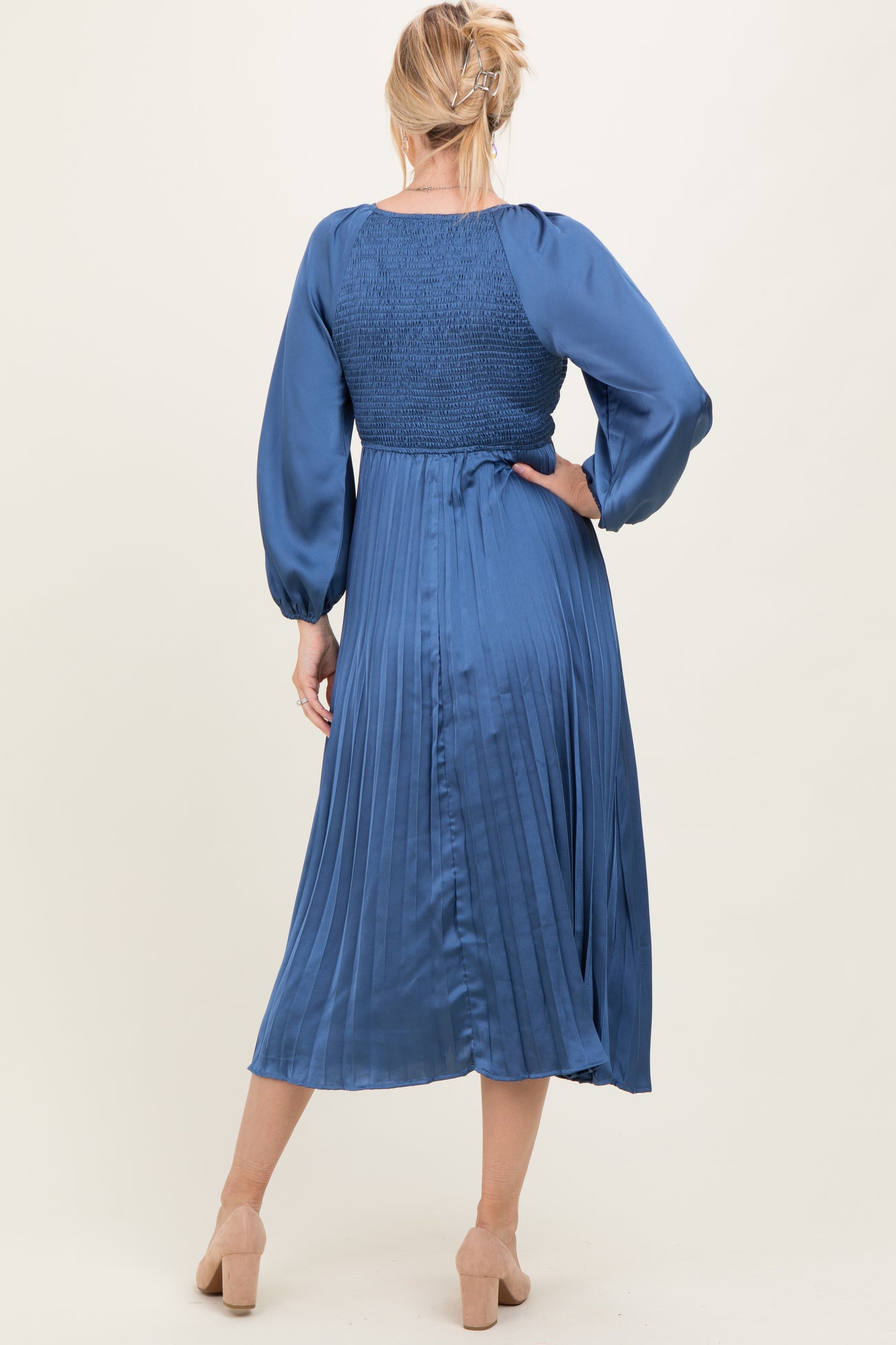 woman wearing a blue pleated midi dress with a smocked bodice and balloon sleeves, seen from the back