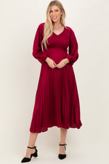 woman wearing a long sleeve burgundy pleated dress with a smocked bodice and flared skirt, posing with hands on her hips