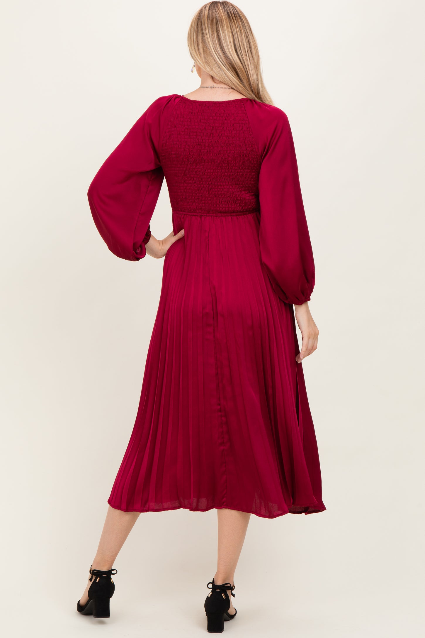woman wearing a burgundy long sleeve pleated dress with a smocked bodice and flowy skirt, shown from the back