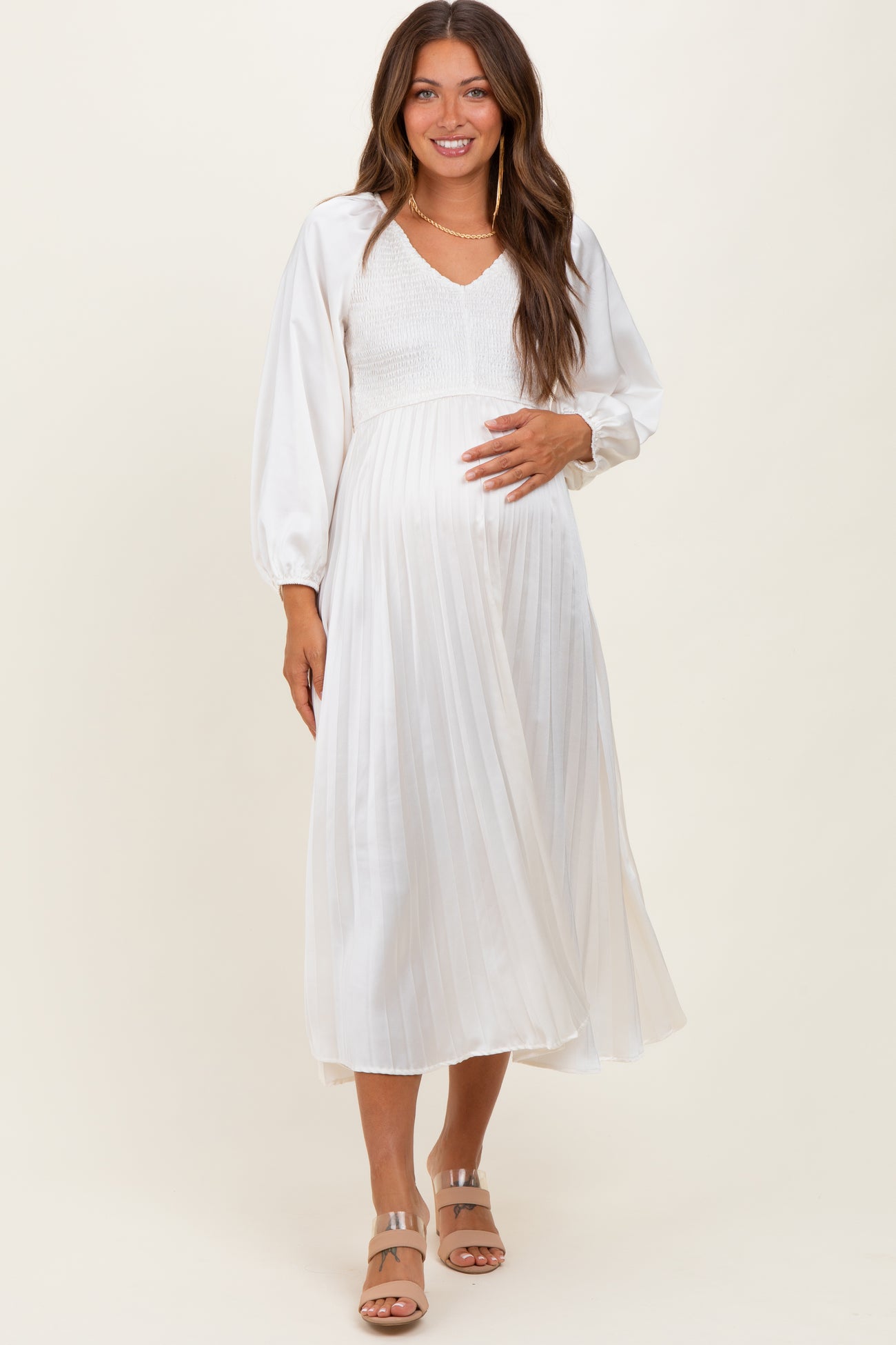 woman wearing a white pleated maternity dress with a v-neck and balloon sleeves, showing her baby bump