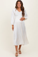 woman wearing a white pleated maternity dress with a v-neck and balloon sleeves, showing her baby bump