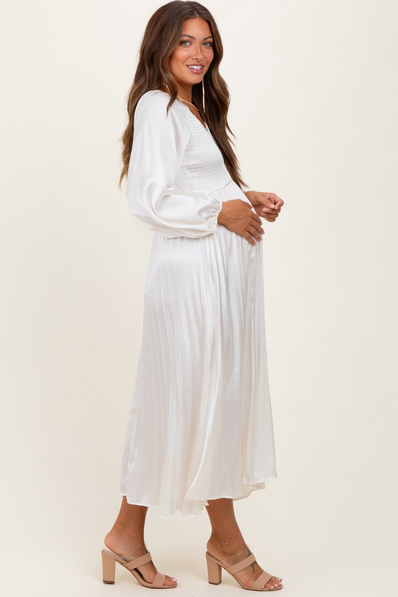 woman wearing a white maternity dress with a smocked bodice and flowy skirt, side view, showcasing a baby bump