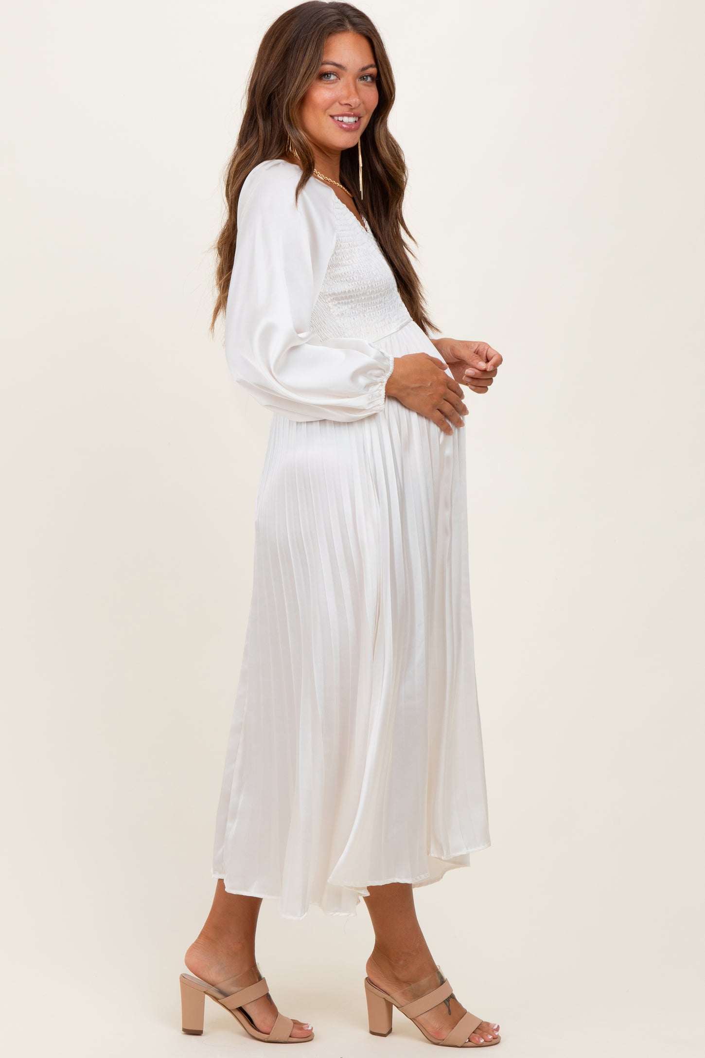 woman wearing a white maternity dress with a smocked bodice and flowy skirt, side view, showcasing a baby bump