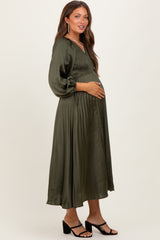 woman wearing an olive green maternity dress with smocked bodice and flowy skirt, gently cradling her baby bump