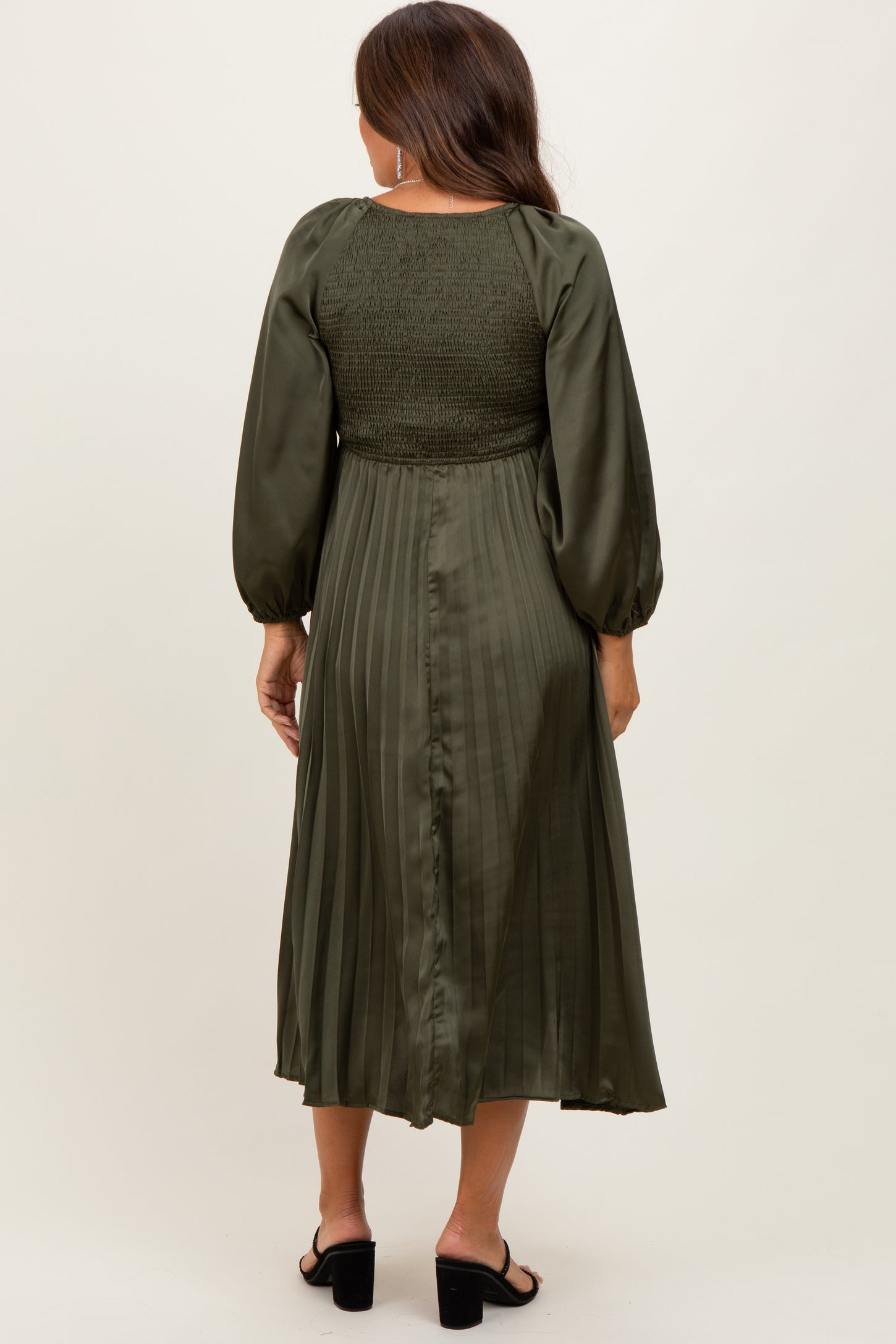 woman wearing a dark green maternity dress with smocked bodice and pleated skirt, showing a baby bump from behind