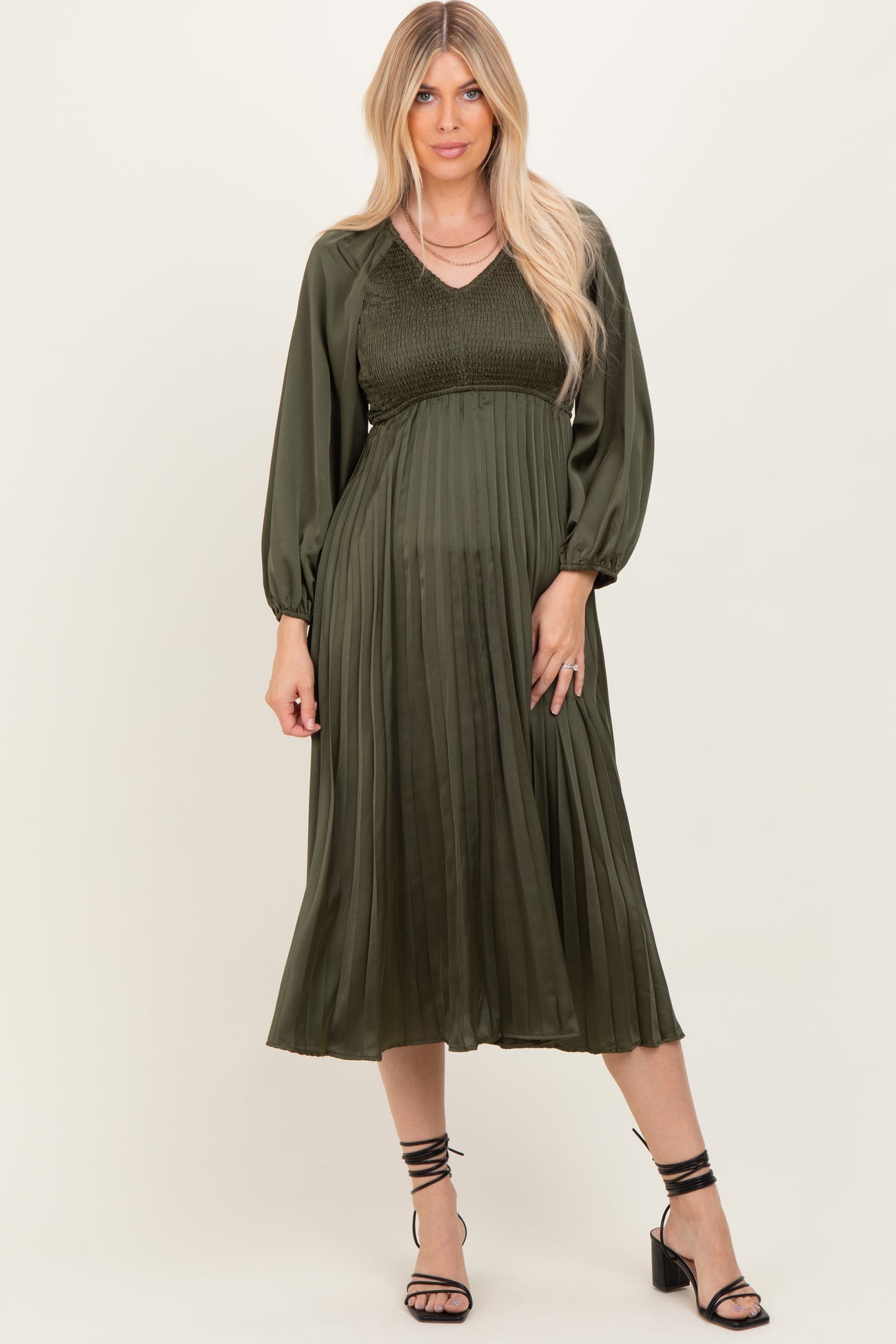 woman wearing an olive green pleated midi dress with puff sleeves and a fitted bodice
