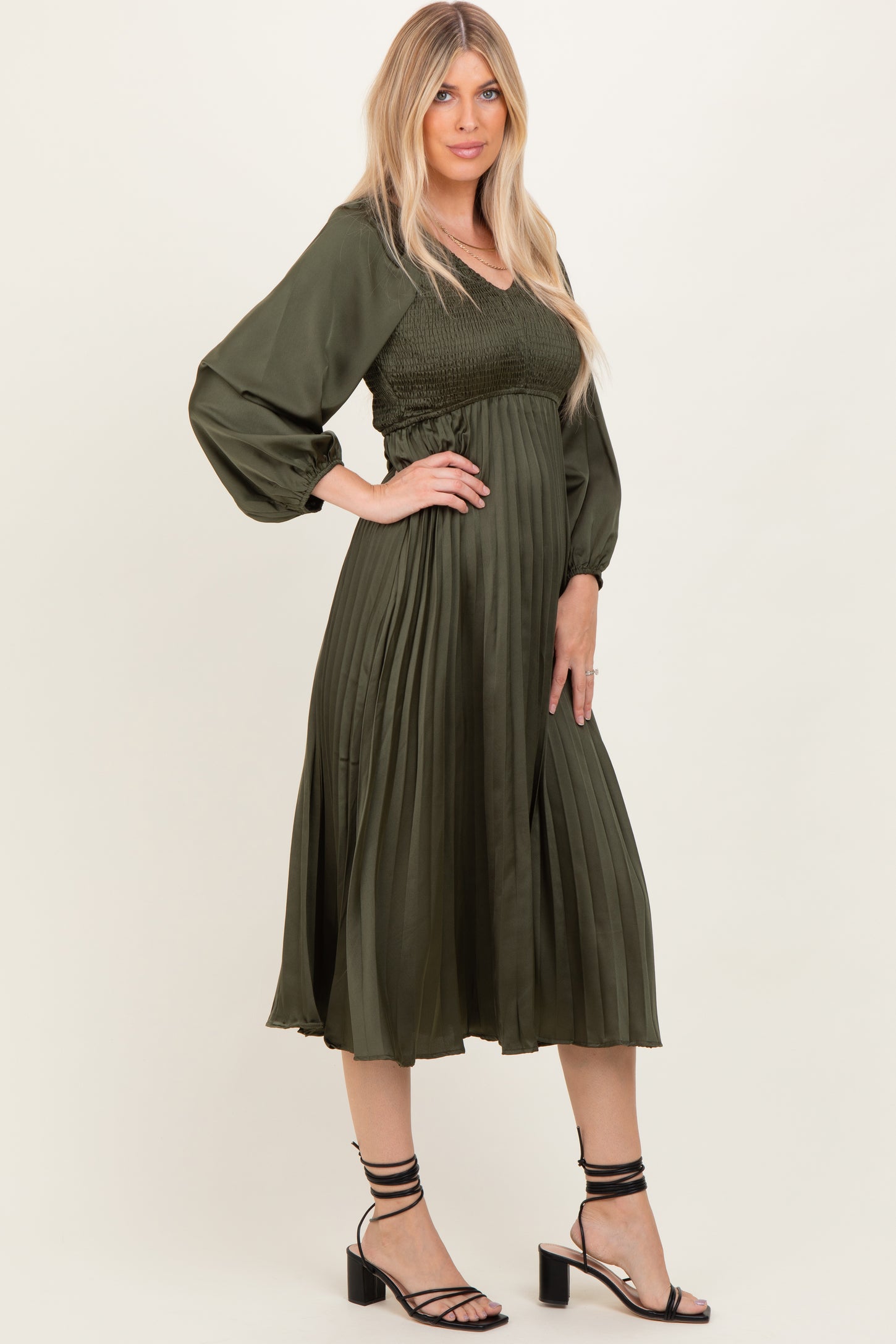 woman wearing a dark green pleated midi dress with a smocked bodice and puff sleeves, styled with strappy heels