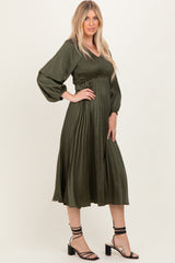 woman wearing a dark green pleated midi dress with a smocked bodice and puff sleeves, styled with strappy heels
