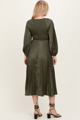 woman wearing an olive green pleated midi dress with a smocked bodice and long sleeves, viewed from the back