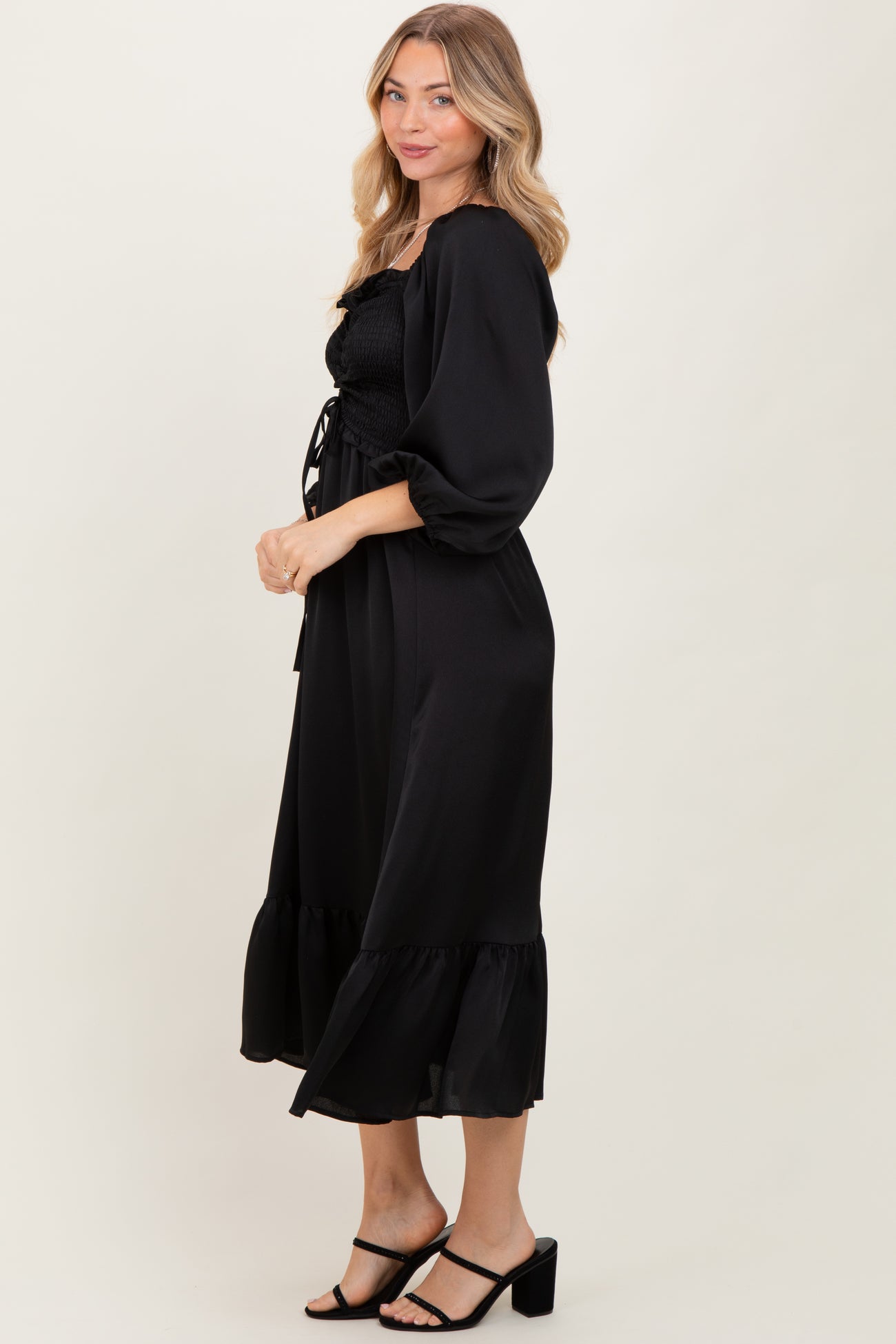 woman wearing a black smocked maxi dress with puff sleeves and a ruffled hem, posed sideways against a neutral background