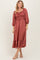 woman wearing a rust-colored midi dress with smocked bodice and puff sleeves, styled with a tiered ruffle hem