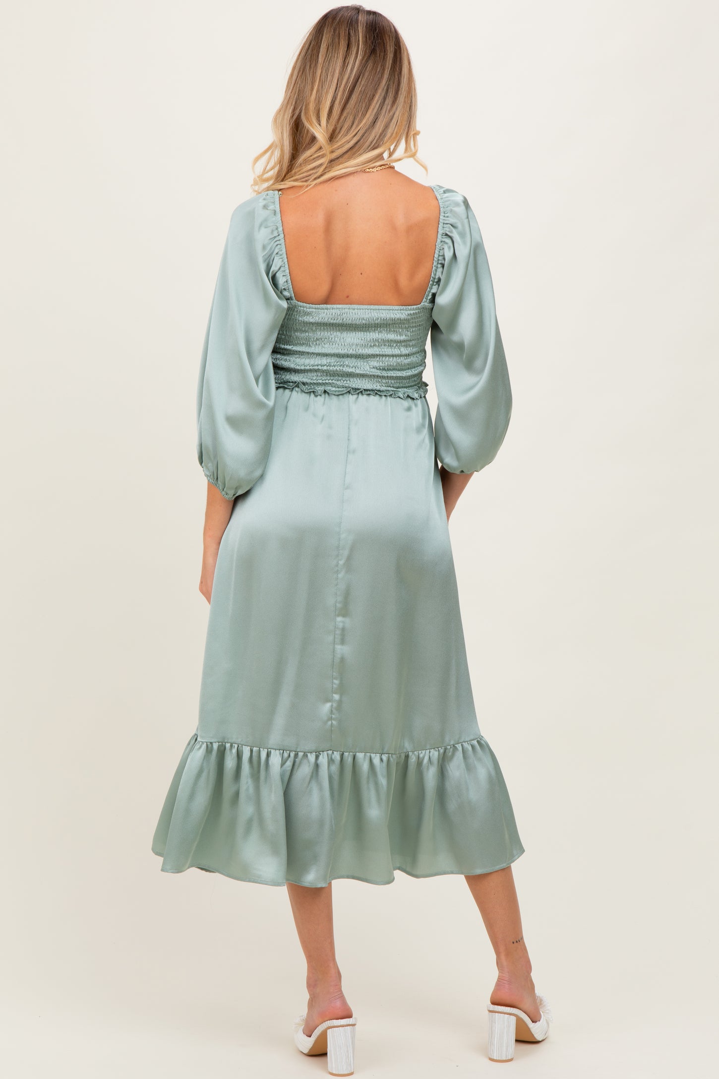 woman wearing a sage green maternity dress with puff sleeves and a smocked back, showcasing a flowing hemline