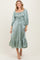 woman wearing a sage green midi dress with smocked bodice and puff sleeves, styled with a ruffled hem