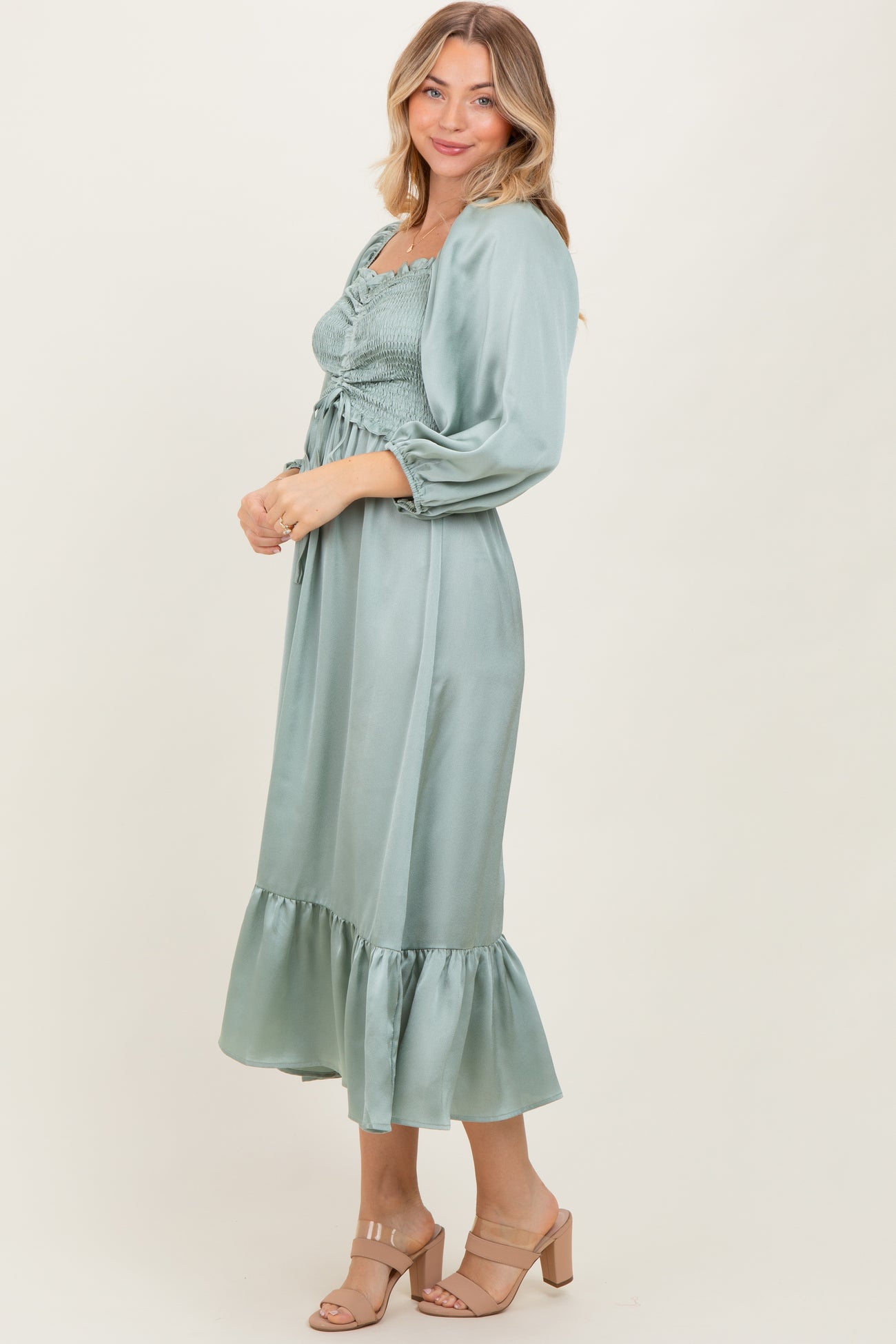 woman wearing a sage green smocked midi dress with ruffled hem and long sleeves