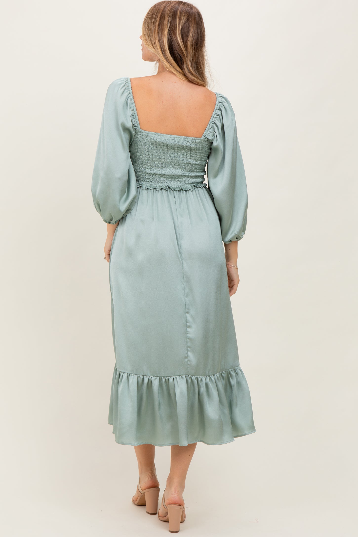woman wearing a sage green backless midi dress with puff sleeves and ruffled hem
